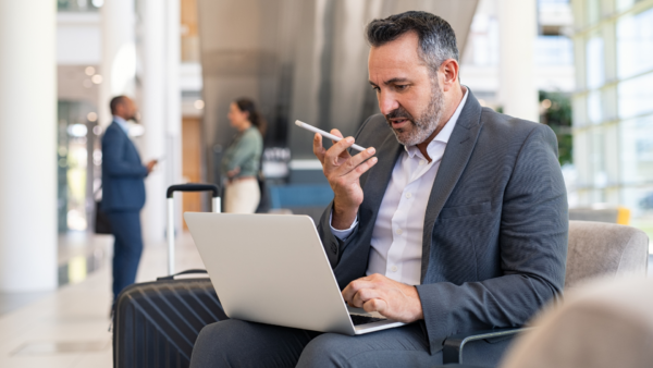 A professional businessman at an airport using a smartphone and laptop, showcasing the convenience of virtual mailbox services for travelers.